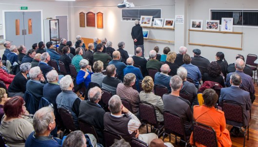 A full house watches Tony Bridge judging prints in the "Movement" category.